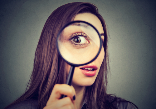 Picture is of a woman looking through a magnifying glass.